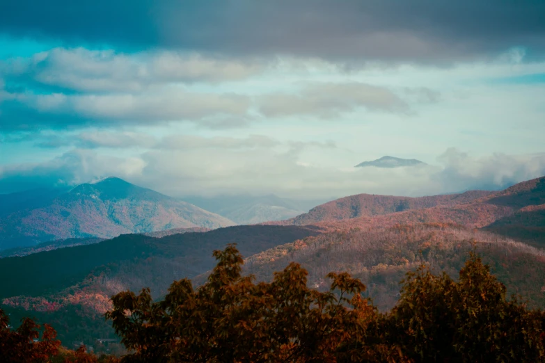 a large tree covered hillside in the middle of a cloudy sky