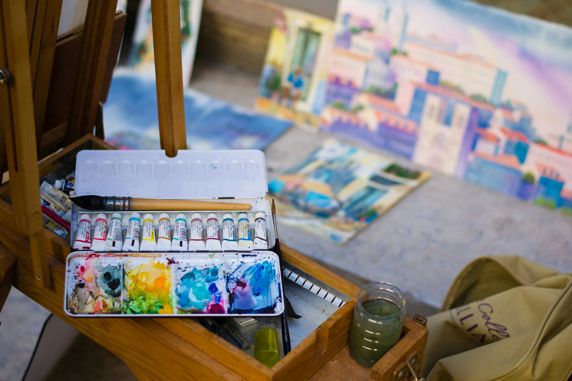 some brushes, paints, and some canvass are on a desk