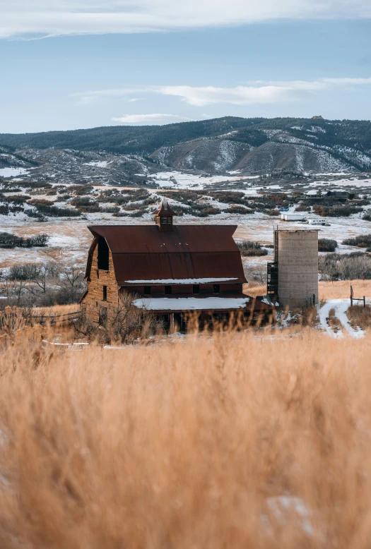 an old abandoned farm house sits in a grassy field with mountains and snow covered hills in the background