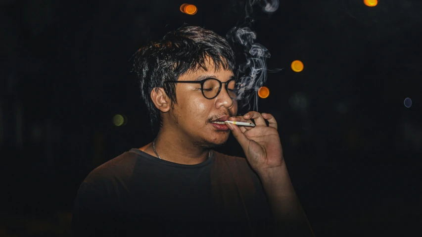 man with glasses on smoking cigarette in the dark