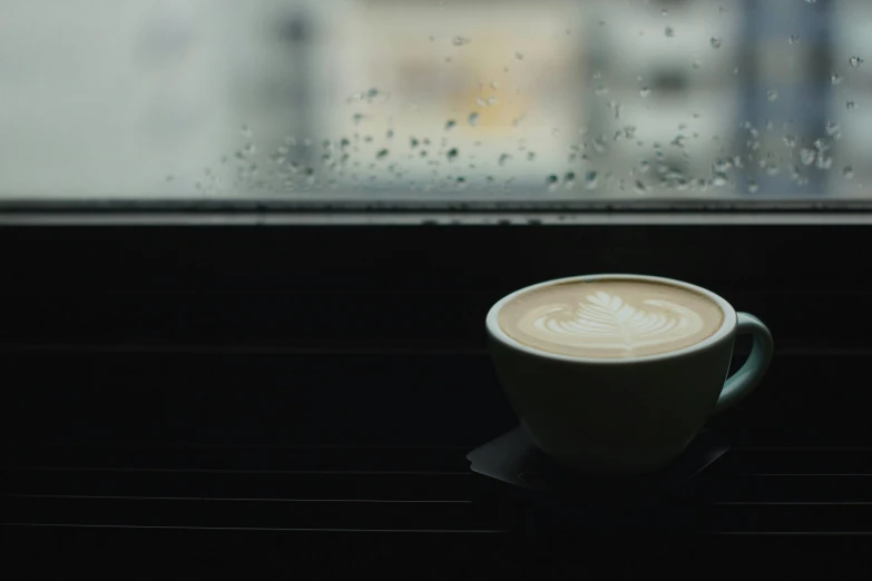 a cappuccino cup sits in the window sill, with rain coming down the window