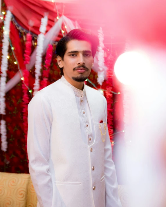 a man wearing a white wedding suit with a pink flower garland