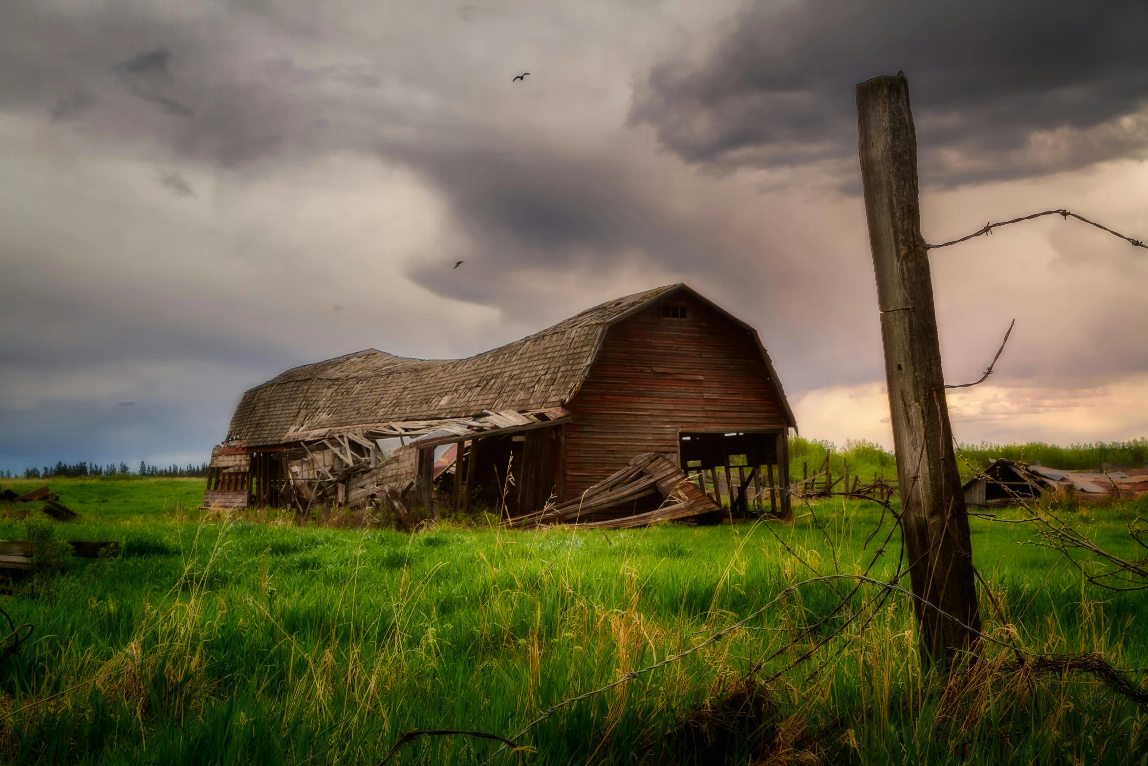 the barn is out on the field and dark clouds are in the background