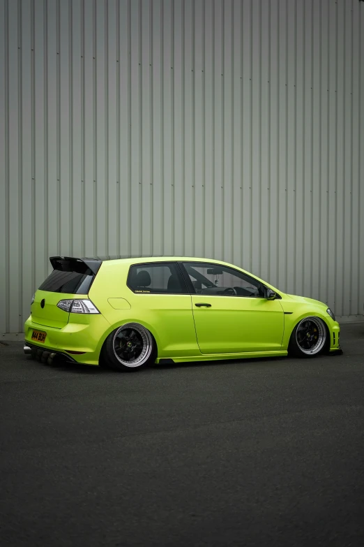 a bright green car with dark chrome wheels parked outside of a building