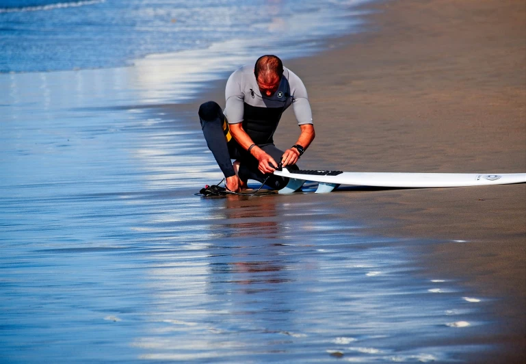 a man in a wet suit and black boots kneeling down while holding a surfboard