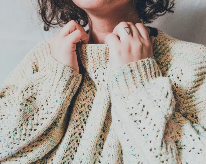 a woman holding onto her sweater while wearing a knitted hand made sweater