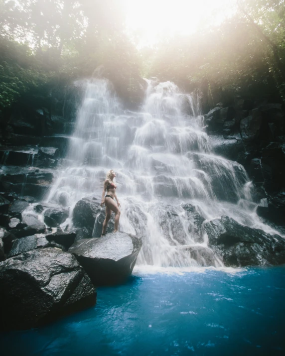 woman sitting on large boulder by flowing pool with waterfall