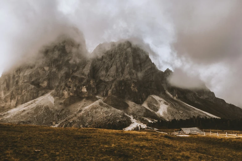 a very tall mountain sitting over a field under a cloudy sky