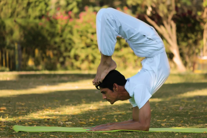 a man in white doing a yoga pose in the park