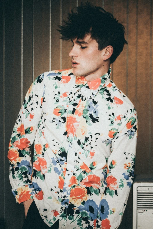 a male with a black hair wearing an floral shirt and earrings