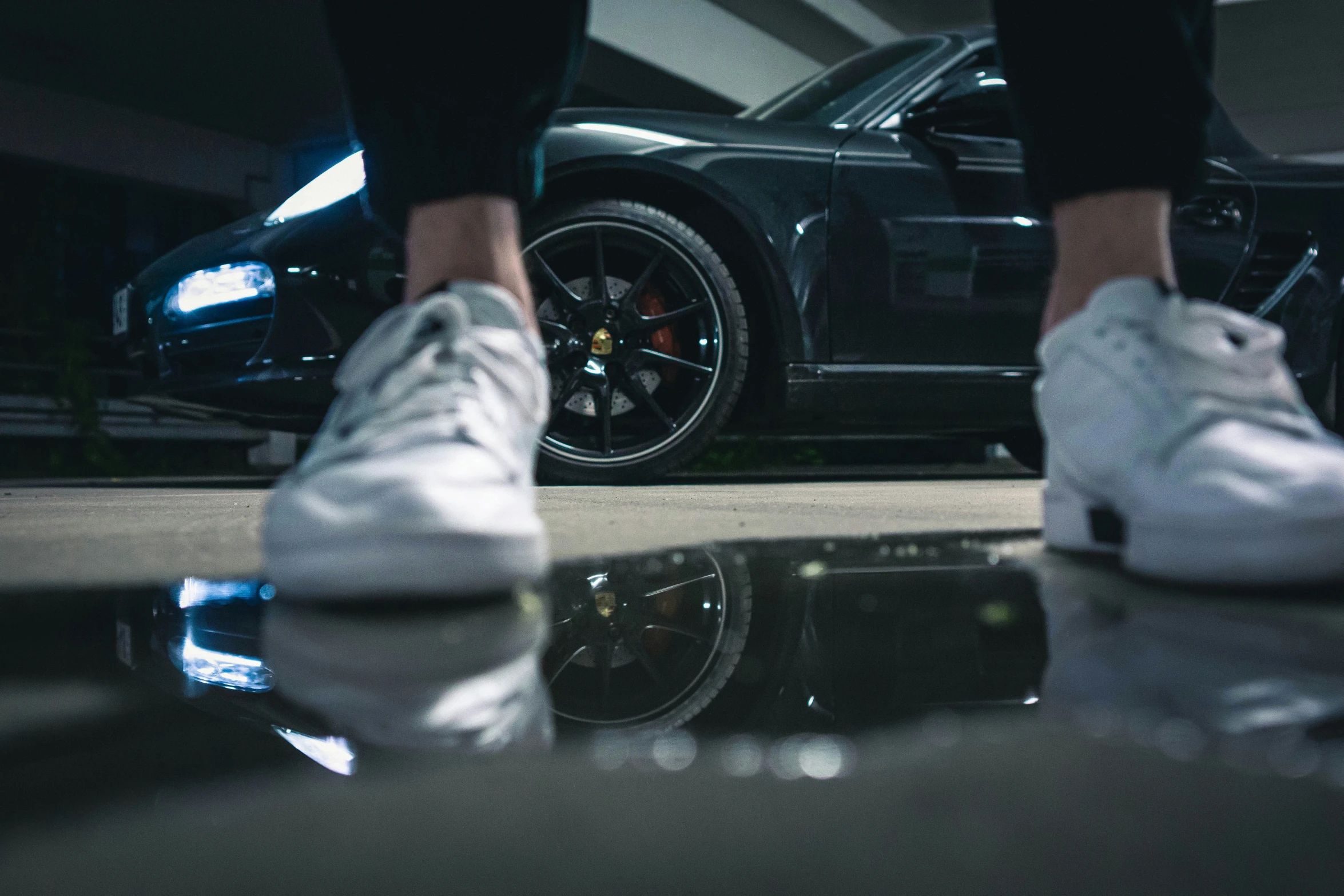 someones feet and ankles wearing white shoes near a black sports car