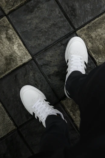 two people wearing white sneakers standing on a tiled floor