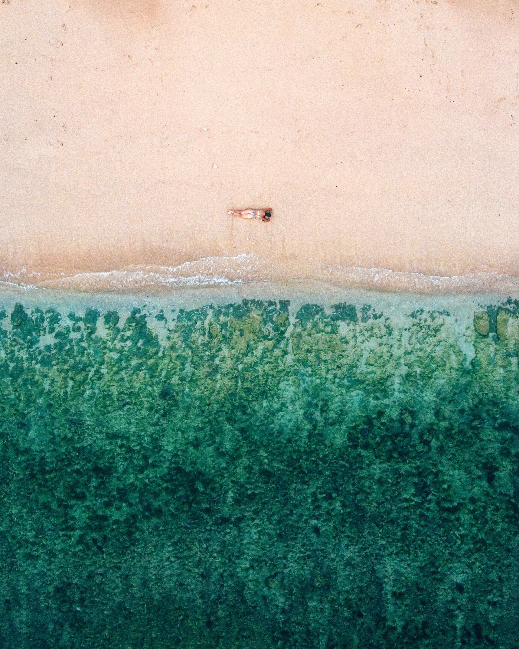 an overhead view of a sandy beach and green water
