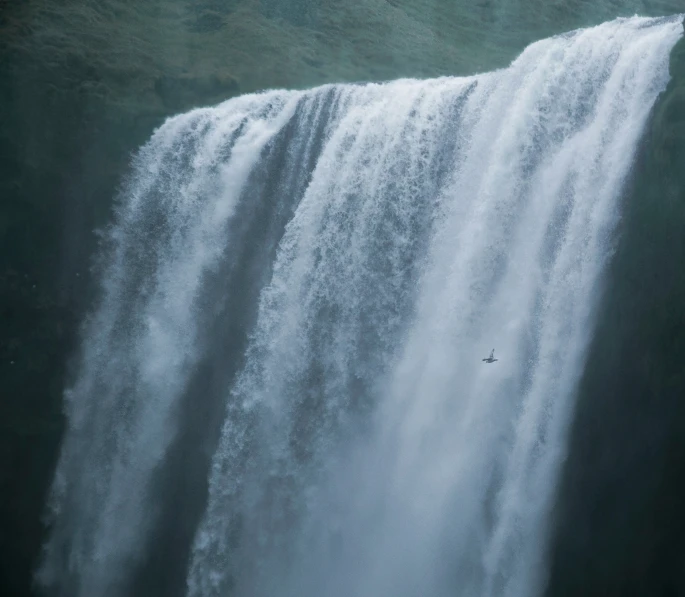 a large waterfall with a single bird in front of it