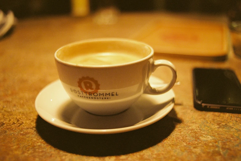 a white cup on a saucer near a phone