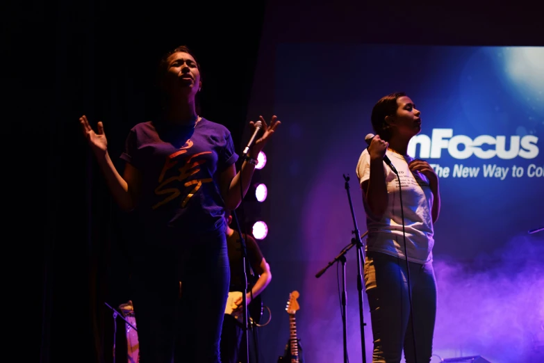 two woman singing on stage with microphones and speakers