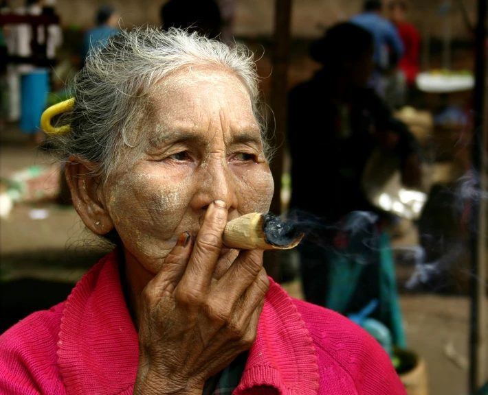 an elderly lady smoking in a market while holding onto a pipe