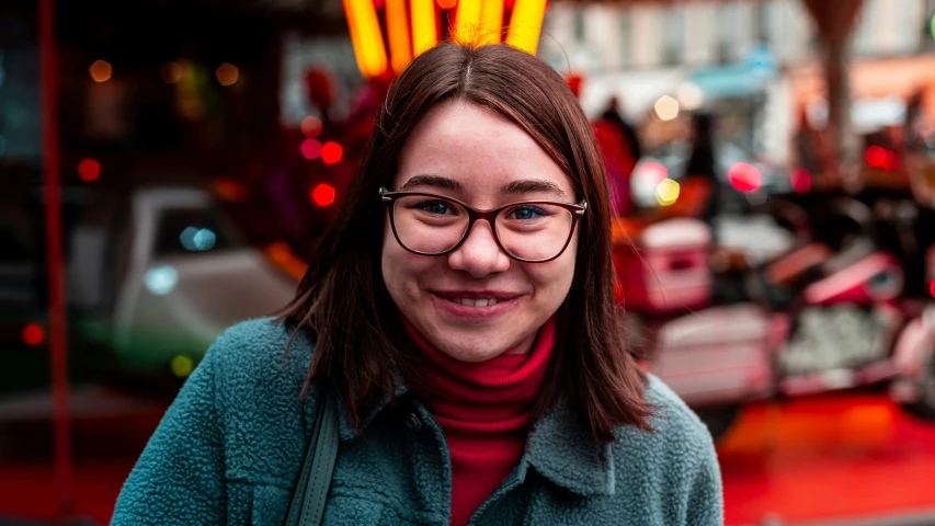 a woman in blue jacket and green sweater next to neon lights