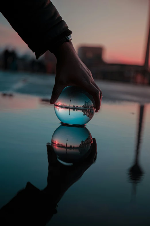 a hand holding onto a round object that is reflecting in the water