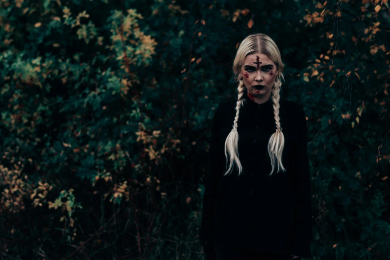 woman with long blond hair and scary make up standing in front of leaves