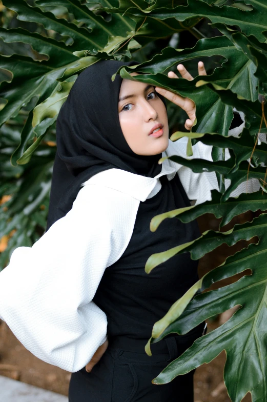 a beautiful woman in a black hijab leaning against a bush