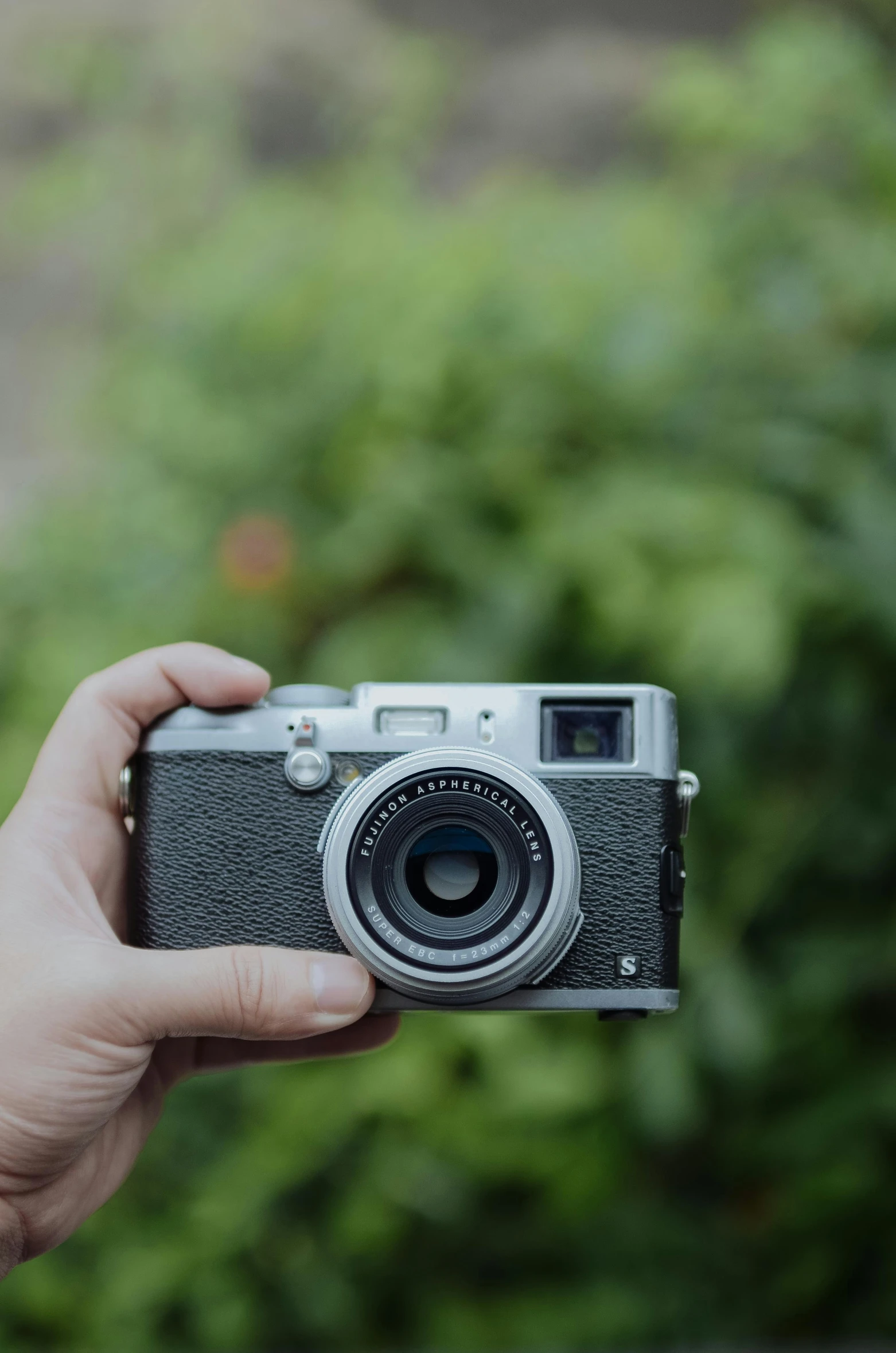 a hand holding up a camera in front of bushes