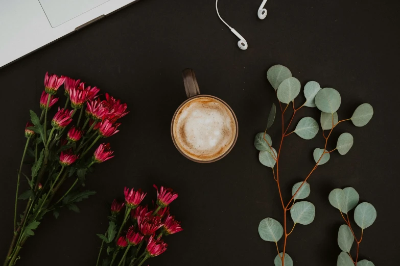 flowers, coffee cup, headphones, head phones and ear buds sit on a black table