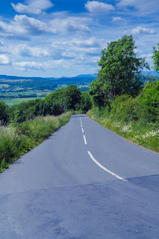 the road is empty as a street sign stands in front of a lush green hillside