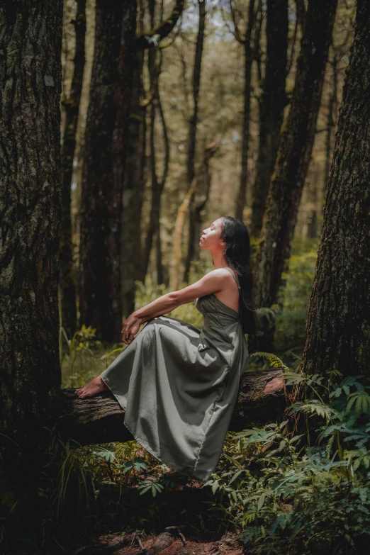 a woman with long hair sitting on a log in a forest