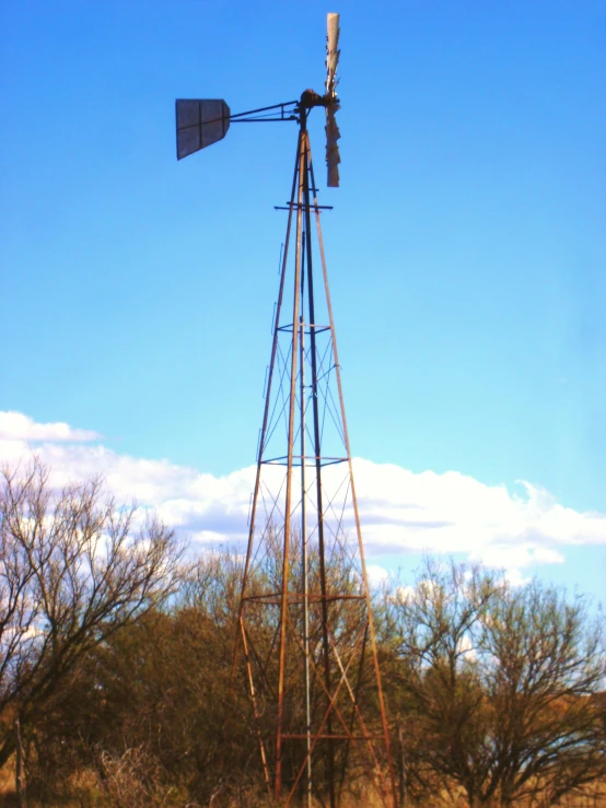 a farm - style windmill sits in the field against a blue sky