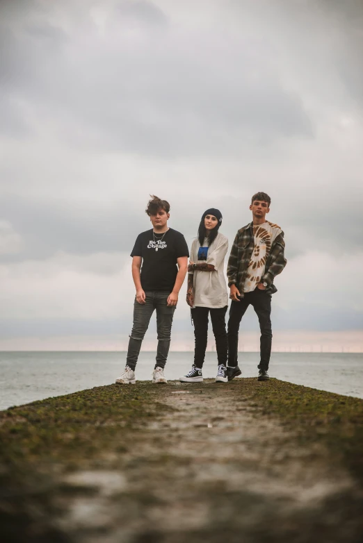 three young men pose for the camera with a body of water in the background