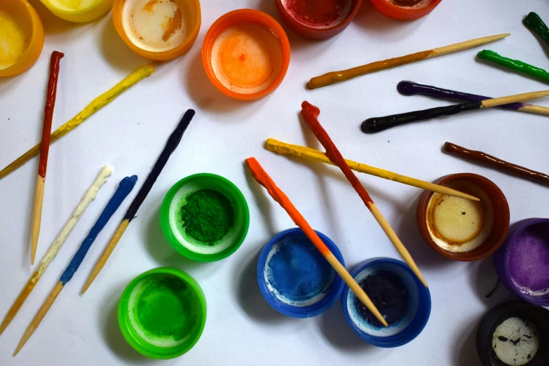 there are many bowls with paint and wooden sticks