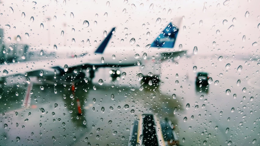 airplanes and luggage planes are parked on the runway through a rain covered window