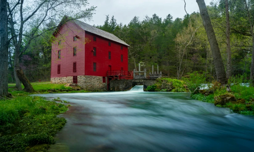 a red mill sits on a creek and houses