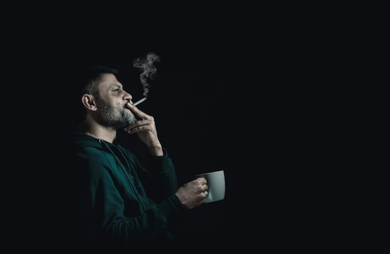 a man smoking a cigarette while holding a cup