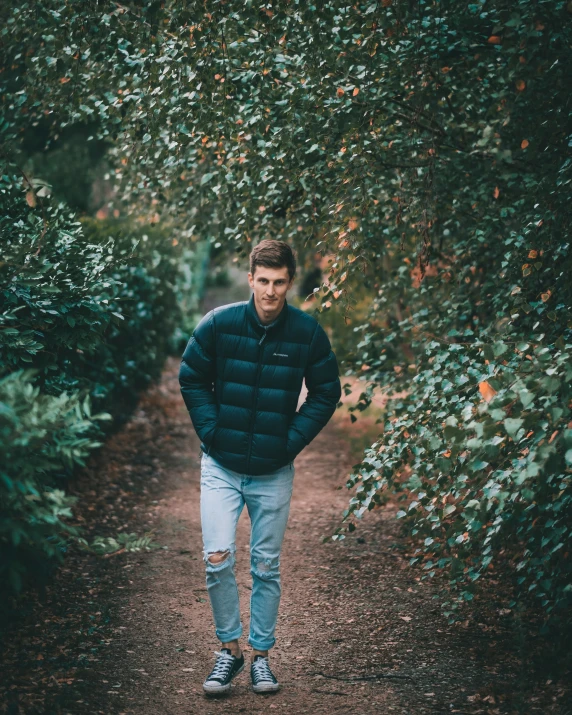 a man wearing blue jacket standing in a wooded path