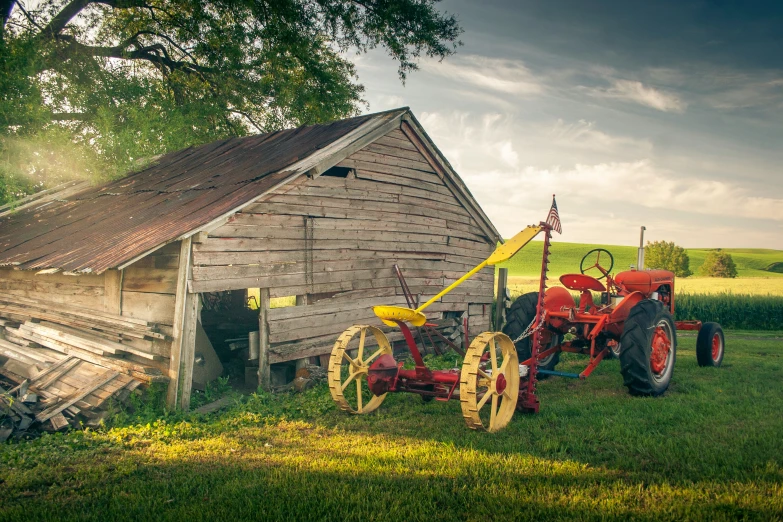 an old wooden farm building with two red tractor parked next to it