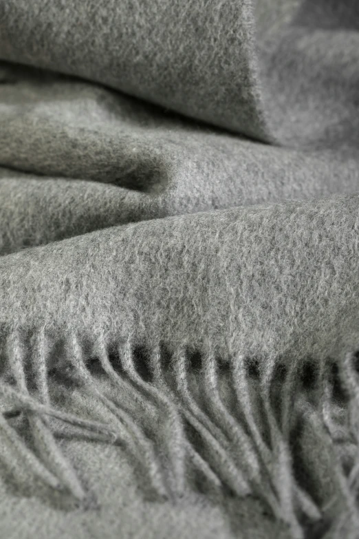 the image shows a close - up of a gray blanket that is made out of wool and with frayed edges