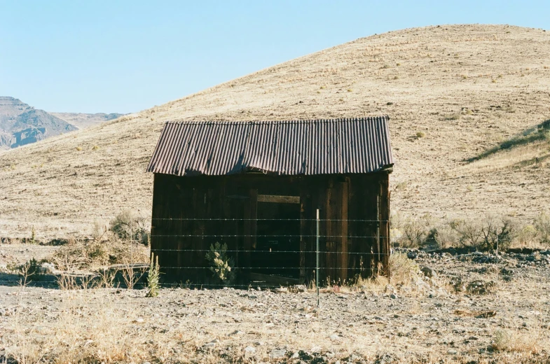 an old shed sitting on top of a dry grass hillside