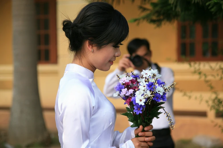 two men taking pictures of a woman holding flowers