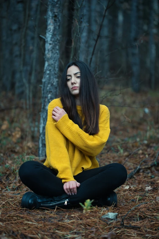 a woman in a yellow sweater is sitting on the ground with her arms folded