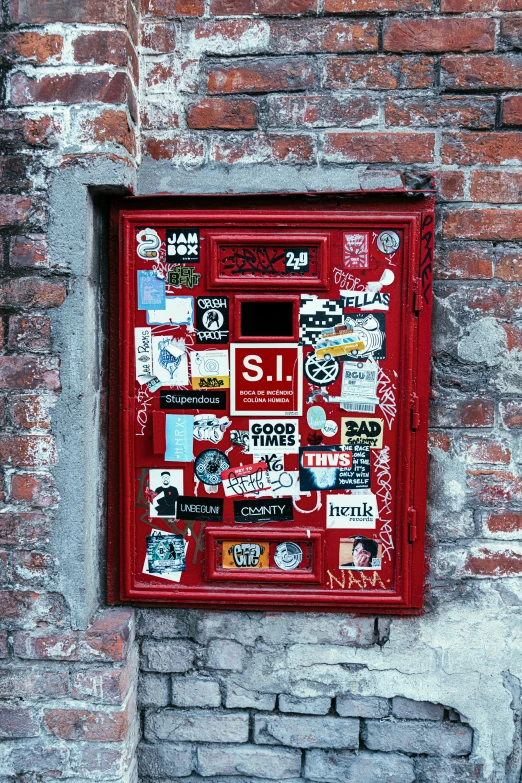 a red mail box on a brick wall that has stickers all over it