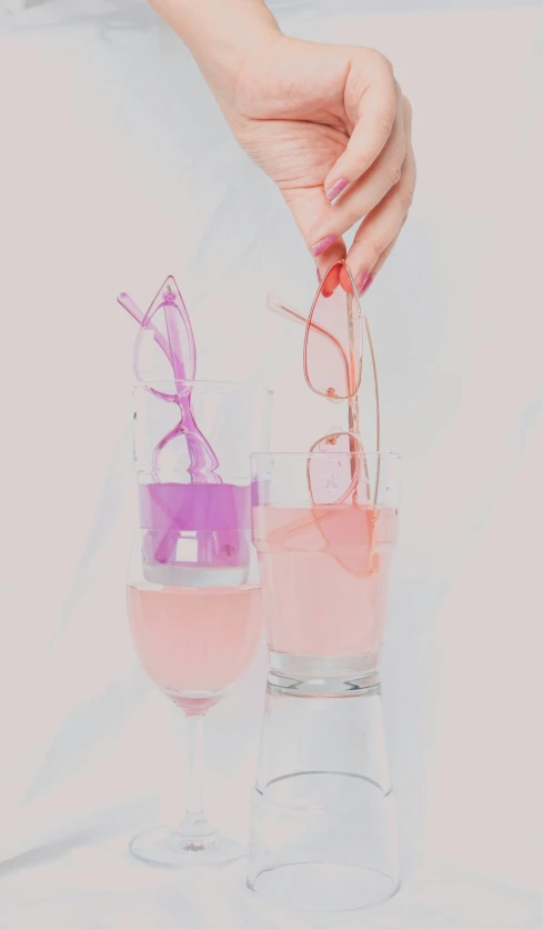 a woman holds a pink colored object out of the water in a glass