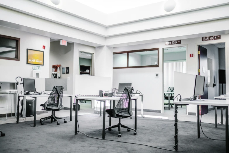 three desks in an empty room with computers