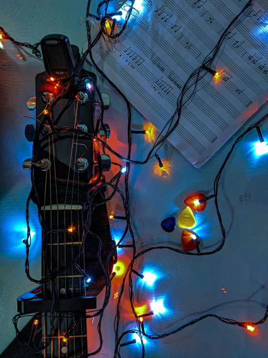 strings and lights hang from the electric guitar and an open sheet of paper laying on top