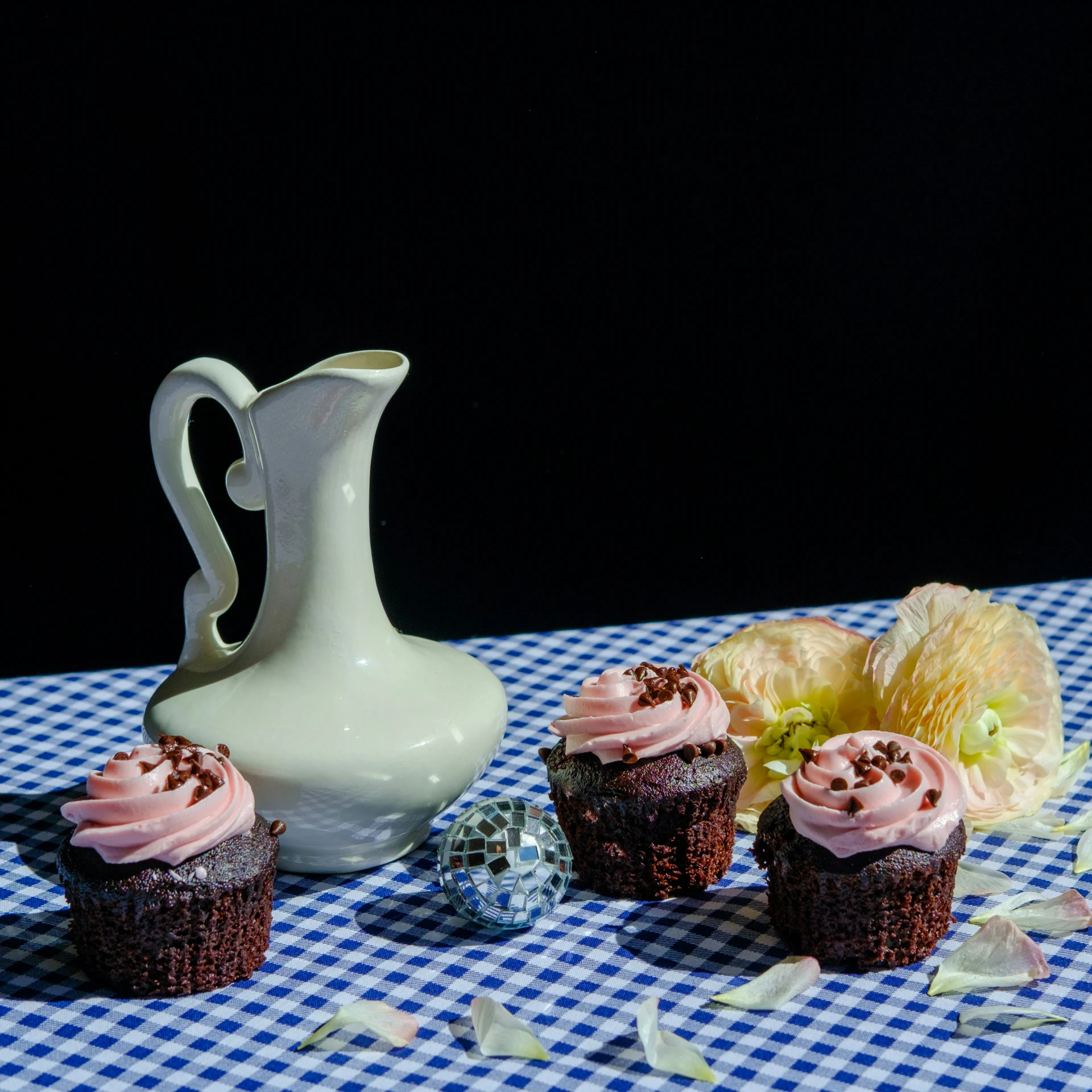 two chocolate cupcakes with pink frosting are arranged next to a creamer