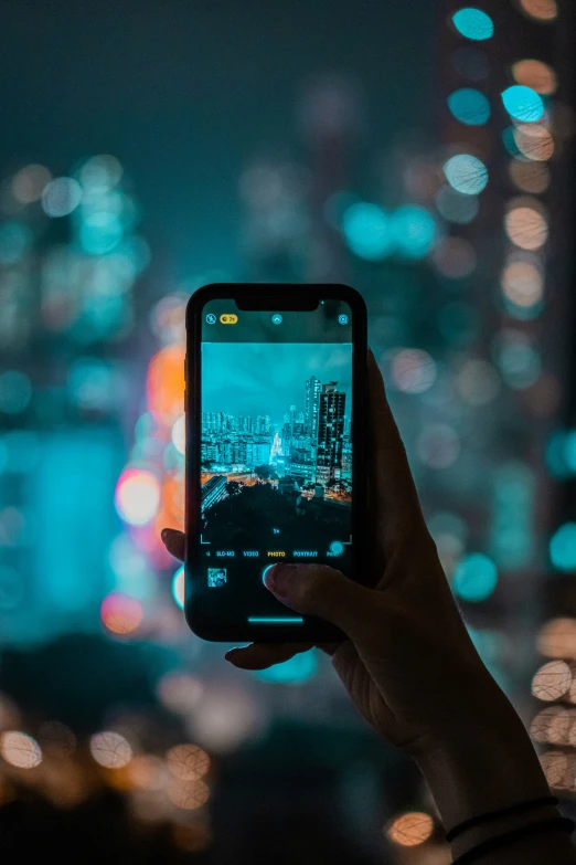 a person's hand holding a smartphone over a city at night