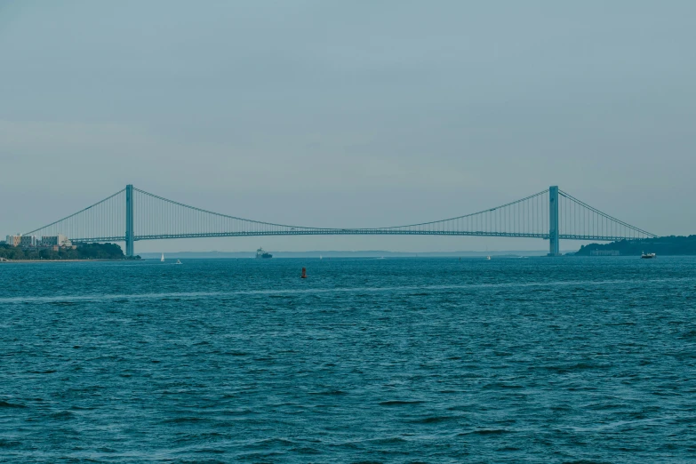 two boats traveling across a body of water under a large bridge