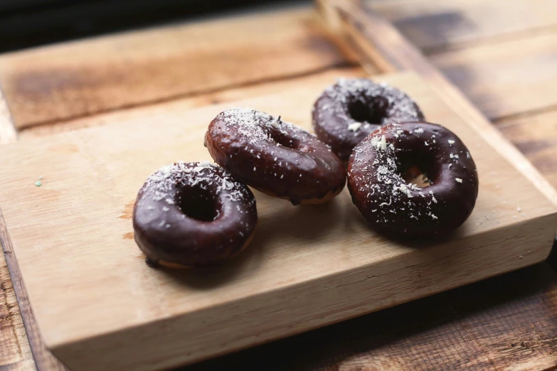 three chocolate donuts with powdered sugar sit on a  board