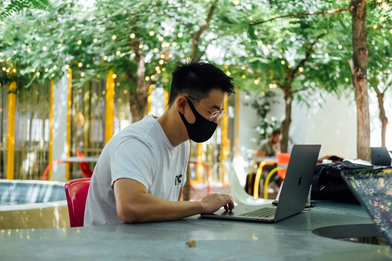 a man wearing a face mask while working on his laptop